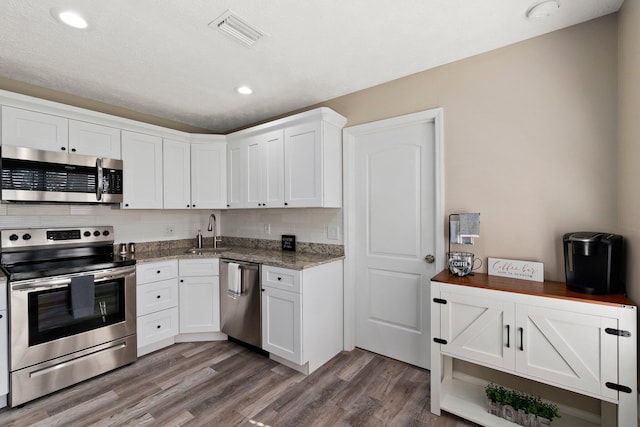 1251 SW Sudder Ave, Port Saint Lucie, FL 34953 - kitchen featuring stainless steel appliances, wood finished floors, white cabinets, light stone counters, and recessed lighting