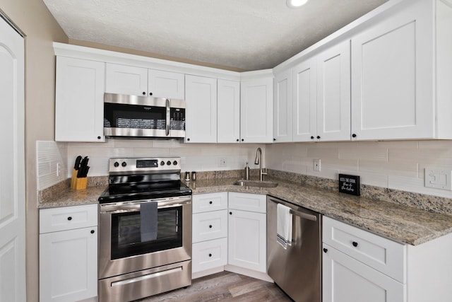 1251 SW Sudder Ave, Port Saint Lucie, FL 34953 - kitchen with stainless steel appliances, tasteful backsplash, white cabinets, light wood-type flooring, and a textured ceiling