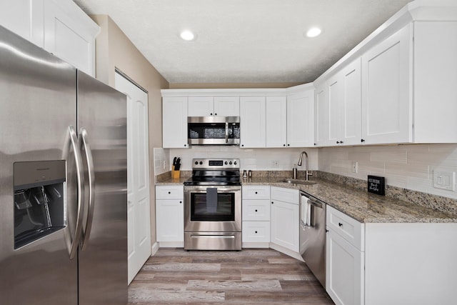 1251 SW Sudder Ave, Port Saint Lucie, FL 34953 - kitchen with appliances with stainless steel finishes, light wood-type flooring, white cabinetry, decorative backsplash, and light stone counters