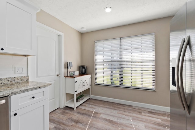 1251 SW Sudder Ave, Port Saint Lucie, FL 34953 - kitchen with stainless steel refrigerator with ice dispenser, light wood finished floors, white cabinetry, light stone counters, and a textured ceiling