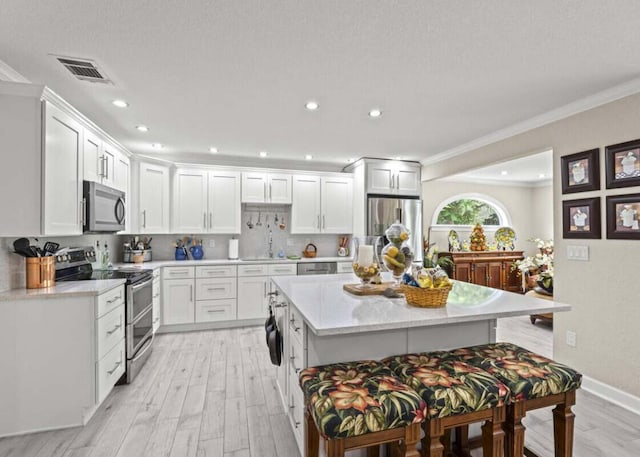 1951 SE Erwin Rd, Port Saint Lucie, FL 34952 - kitchen featuring appliances with stainless steel finishes, light wood-type flooring, light countertops, a kitchen island, and crown molding