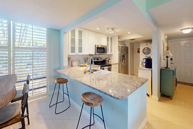 3492 NE Causeway Blvd Unit 104, Jensen Beach, FL 34957 - kitchen featuring appliances with stainless steel finishes, light tile patterned floors, light stone counters, a breakfast bar, and a peninsula