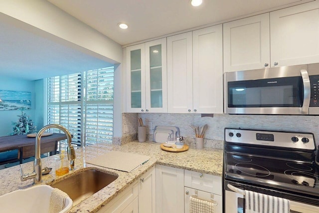 3492 NE Causeway Blvd Unit 104, Jensen Beach, FL 34957 - kitchen featuring appliances with stainless steel finishes, white cabinets, glass insert cabinets, light stone countertops, and recessed lighting