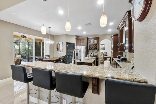 12358 Saint Simon Dr, Boca Raton, FL 33428 - kitchen with an island with sink, light stone countertops, pendant lighting, a kitchen breakfast bar, and glass insert cabinets