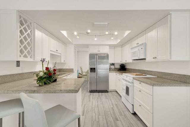 3824 SE Fairway E, Stuart, FL 34997 - kitchen featuring white appliances, a peninsula, a raised ceiling, white cabinetry, and light stone countertops