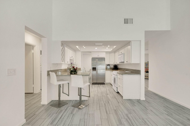3824 SE Fairway E, Stuart, FL 34997 - kitchen featuring white appliances, a peninsula, a kitchen bar, wood finish floors, and a towering ceiling