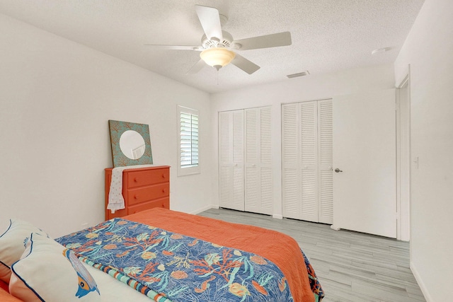 3824 SE Fairway E, Stuart, FL 34997 - bedroom featuring light wood finished floors, two closets, a textured ceiling, and ceiling fan