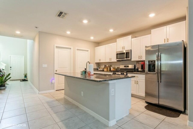 5126 Dandelion St, Apollo Beach, FL 33572 - kitchen with stainless steel appliances, light tile patterned floors, an island with sink, dark stone counters, and white cabinetry