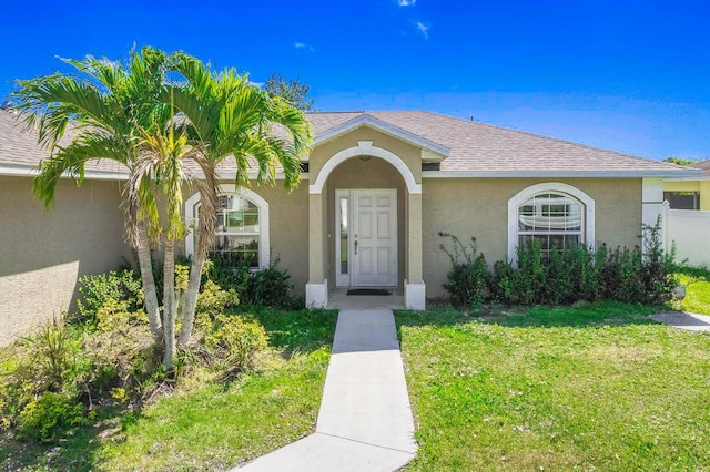 5533 NW Cordrey St, Port Saint Lucie, FL 34986 - view of exterior entry featuring a yard, stucco siding, and roof with shingles