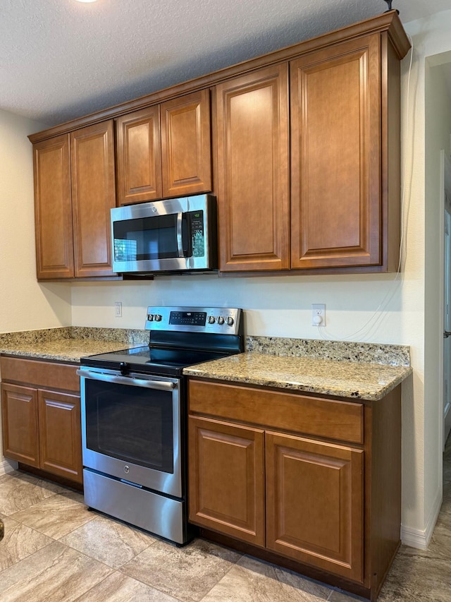 2313 SW Neal Rd, Port Saint Lucie, FL 34953 - kitchen featuring stainless steel appliances, brown cabinetry, light stone counters, and a textured ceiling