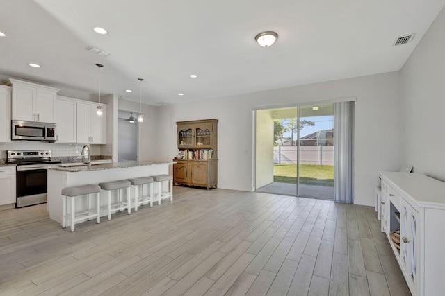 774 SE Ablett Ln, Port Saint Lucie, FL 34984 - kitchen featuring appliances with stainless steel finishes, tasteful backsplash, a kitchen bar, a kitchen island with sink, and light wood finished floors