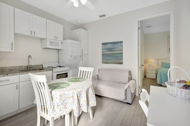774 SE Ablett Ln, Port Saint Lucie, FL 34984 - kitchen with stacked washer / drying machine, white appliances, light wood-style flooring, white cabinets, and a ceiling fan