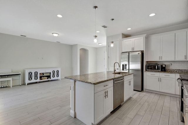 774 SE Ablett Ln, Port Saint Lucie, FL 34984 - kitchen featuring arched walkways, appliances with stainless steel finishes, light wood-type flooring, dark stone countertops, and white cabinetry