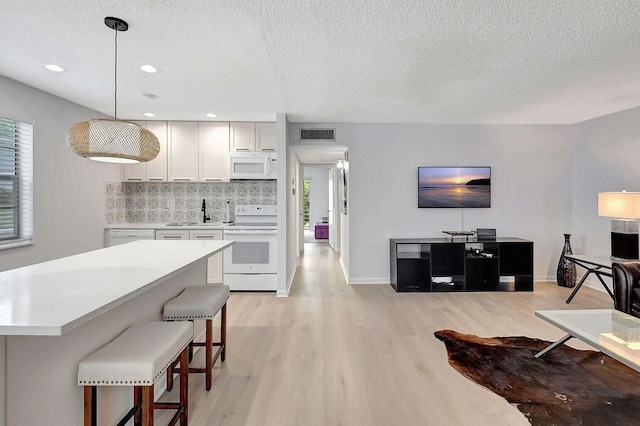 74 Normandy Unit B, Delray Beach, FL 33484 - kitchen featuring white appliances, light wood finished floors, light countertops, a breakfast bar, and a textured ceiling