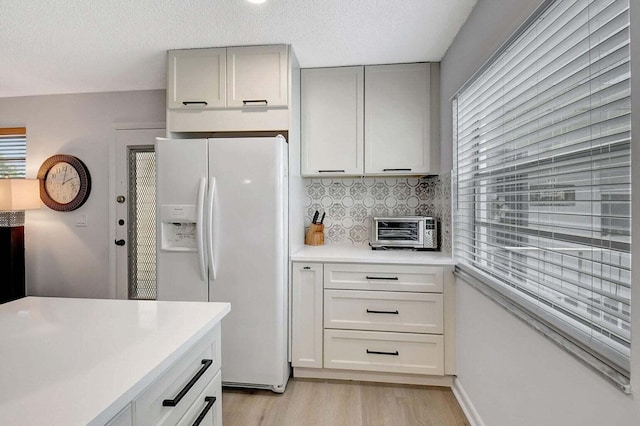 74 Normandy Unit B, Delray Beach, FL 33484 - kitchen with white fridge with ice dispenser, light wood-style flooring, light countertops, decorative backsplash, and a textured ceiling
