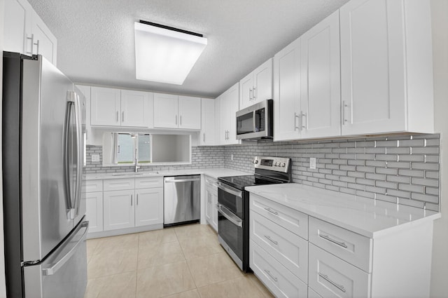 5574 Witney Dr Unit 104, Delray Beach, FL 33484 - kitchen featuring appliances with stainless steel finishes, backsplash, a textured ceiling, white cabinetry, and light tile patterned floors