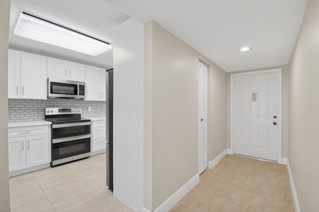 5574 Witney Dr Unit 104, Delray Beach, FL 33484 - kitchen with appliances with stainless steel finishes, light countertops, light tile patterned floors, backsplash, and white cabinets