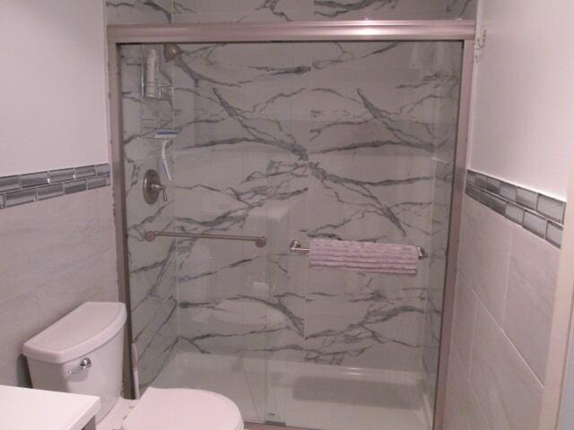 14572 Canalview Dr Unit C, Delray Beach, FL 33484 - bathroom featuring tile walls, a marble finish shower, vanity, and a wainscoted wall