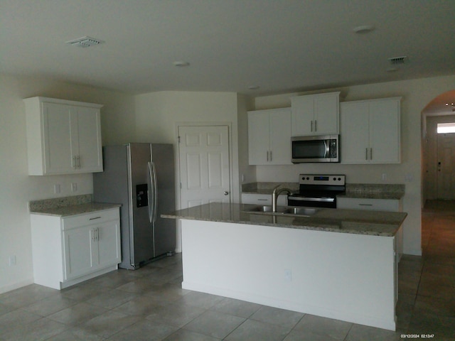 10574 SW Jem St, Port Saint Lucie, FL 34987 - kitchen with stainless steel appliances, an island with sink, white cabinetry, and light stone counters
