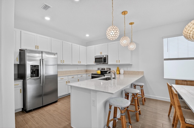 14929 Three Ponds Trl, Delray Beach, FL 33446 - kitchen with stainless steel appliances, a peninsula, a breakfast bar, light wood-type flooring, and white cabinetry