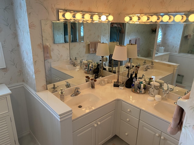 3053 SE Darien Rd, Port Saint Lucie, FL 34952 - bathroom featuring wallpapered walls, double vanity, and wainscoting