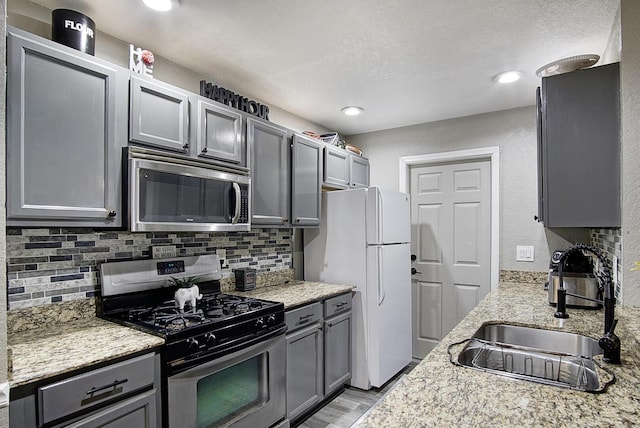 372 NE Ardsley Dr, Port Saint Lucie, FL 34983 - kitchen with appliances with stainless steel finishes, gray cabinetry, decorative backsplash, light wood-style flooring, and a textured ceiling