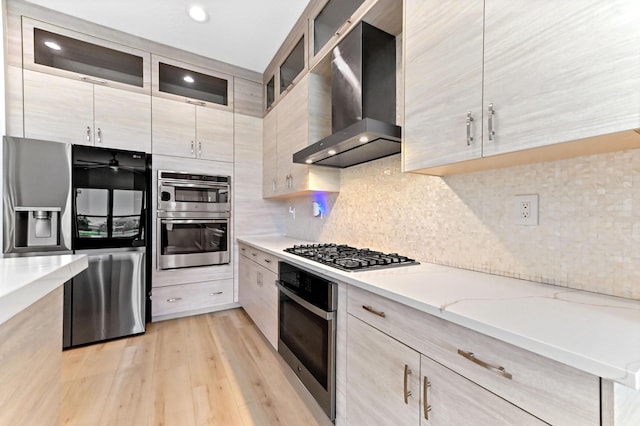 17380 Rainstream Rd, Boca Raton, FL 33496 - kitchen featuring appliances with stainless steel finishes, wall chimney range hood, light wood finished floors, decorative backsplash, and light stone counters