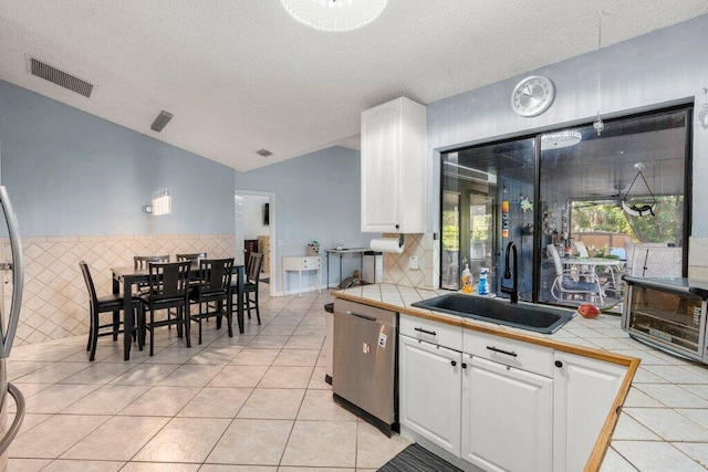 2997 SW Collings Dr, Port Saint Lucie, FL 34953 - kitchen with stainless steel dishwasher, tile counters, white cabinetry, lofted ceiling, and a textured ceiling
