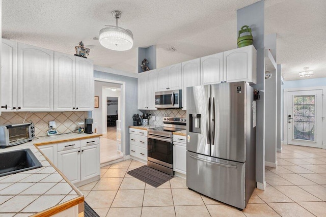 2997 SW Collings Dr, Port Saint Lucie, FL 34953 - kitchen featuring stainless steel appliances, tile counters, a textured ceiling, light tile patterned floors, and white cabinetry