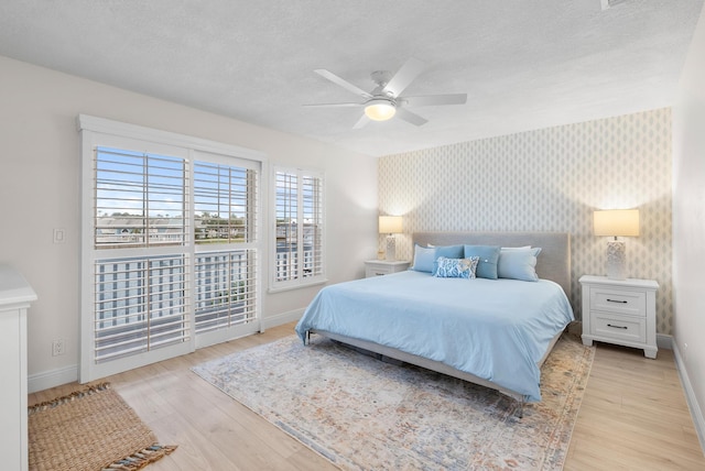 1219 Ocean Dunes Cir, Jupiter, FL 33477 - bedroom with wallpapered walls, an accent wall, light wood-style floors, a textured ceiling, and ceiling fan