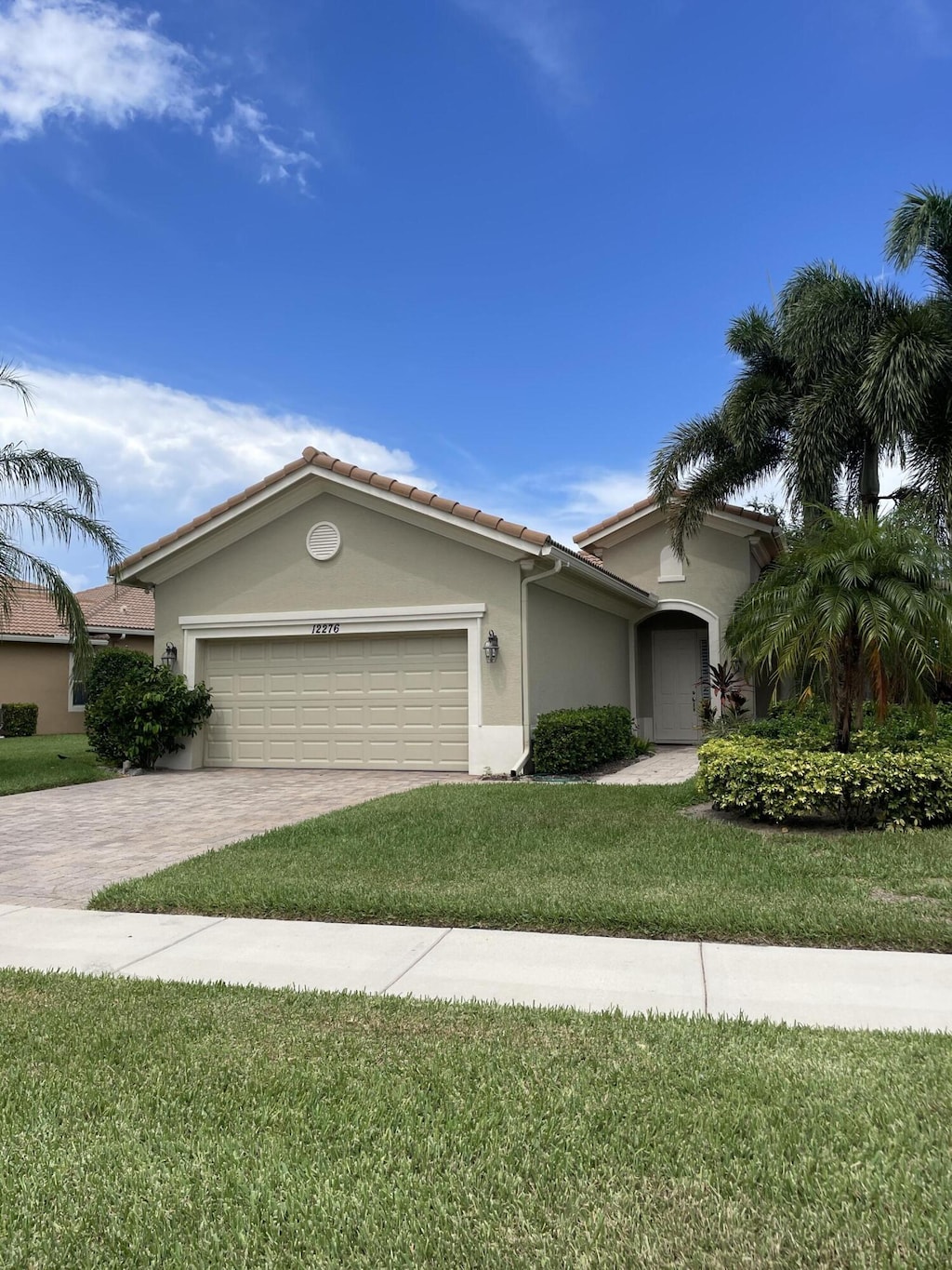 12276 Aviles Cir, Palm Beach Gardens, FL 33418 - view of front of home with stucco siding, a garage, driveway, a front yard, and a tiled roof