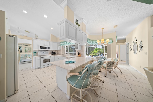 1104 SE Strathmore Dr, Port Saint Lucie, FL 34952 - kitchen featuring white appliances, a chandelier, light tile patterned floors, light countertops, and a peninsula
