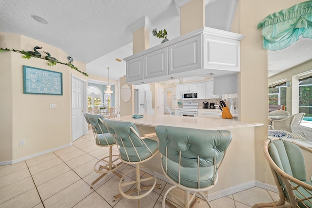 1104 SE Strathmore Dr, Port Saint Lucie, FL 34952 - kitchen with white appliances, light tile patterned floors, white cabinetry, a kitchen breakfast bar, and a textured ceiling