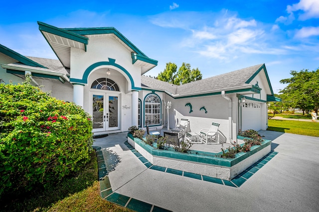 1104 SE Strathmore Dr, Port Saint Lucie, FL 34952 - view of front of house featuring french doors, an attached garage, stucco siding, a shingled roof, and driveway