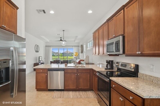 9155 SW Michele Way, Port Saint Lucie, FL 34987 - kitchen featuring stainless steel appliances, a peninsula, ceiling fan, brown cabinetry, and light stone countertops