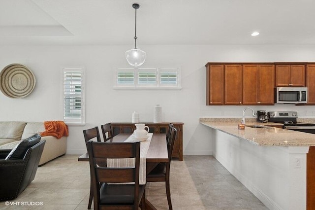 9155 SW Michele Way, Port Saint Lucie, FL 34987 - kitchen with stainless steel appliances, brown cabinetry, light stone counters, a peninsula, and hanging light fixtures