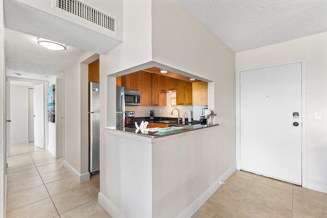 1830 Embassy Dr Unit 401, West Palm Beach, FL 33401 - kitchen with stainless steel appliances, a textured ceiling, light tile patterned floors, brown cabinetry, and dark countertops