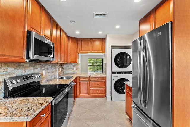 24 Stratford Dr Unit F, Boynton Beach, FL 33436 - kitchen featuring appliances with stainless steel finishes, stacked washer and clothes dryer, brown cabinetry, tasteful backsplash, and light stone counters