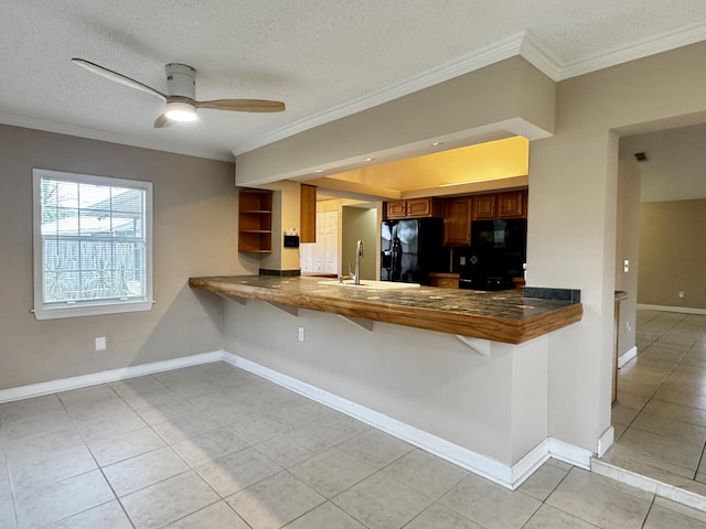610 SE Forgal St, Port Saint Lucie, FL 34983 - kitchen with black appliances, brown cabinets, ornamental molding, light tile patterned floors, and a kitchen breakfast bar