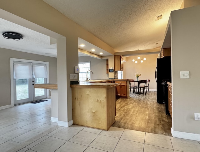 610 SE Forgal St, Port Saint Lucie, FL 34983 - kitchen featuring a textured ceiling, a peninsula, light tile patterned floors, brown cabinets, and freestanding refrigerator