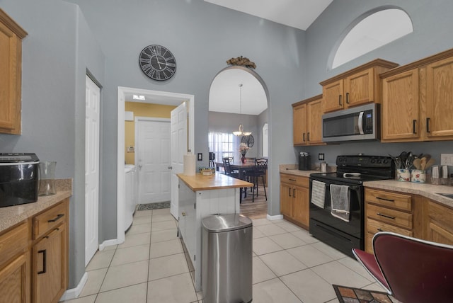 3982 SW Kabane St, Port Saint Lucie, FL 34953 - kitchen featuring electric range, stainless steel microwave, washer and clothes dryer, light countertops, and brown cabinetry