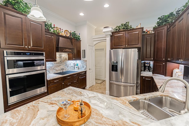 5927 NW Favian Ave, Port Saint Lucie, FL 34986 - kitchen with appliances with stainless steel finishes, custom exhaust hood, dark brown cabinetry, decorative backsplash, and ornamental molding