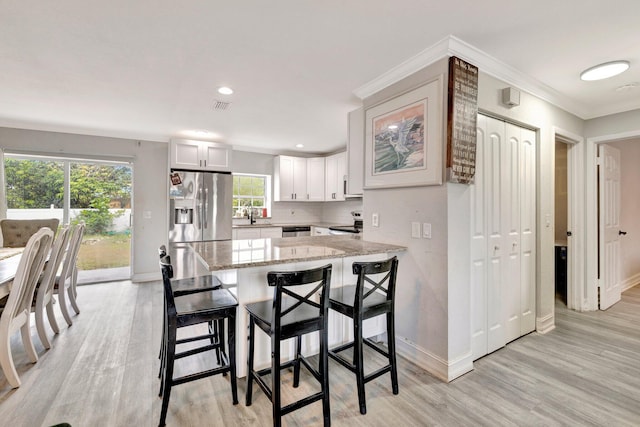 557 SW Violet Ave, Port Saint Lucie, FL 34983 - kitchen with stainless steel appliances, light wood finished floors, a peninsula, light stone counters, and ornamental molding