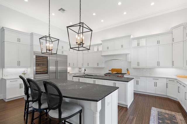 1257 Breakers W Blvd, West Palm Beach, FL 33411 - kitchen featuring a kitchen island with sink, crown molding, built in refrigerator, a chandelier, and backsplash