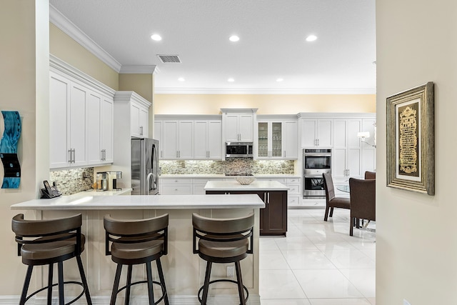8271 Green Mountain Rd, Boynton Beach, FL 33473 - kitchen with stainless steel appliances, a peninsula, a breakfast bar, decorative backsplash, and light countertops