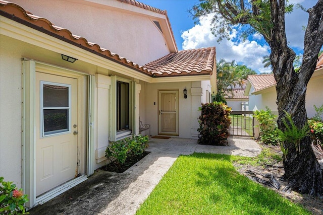 2646 Mohawk Cir, West Palm Beach, FL 33409 - doorway to property featuring a tiled roof, stucco siding, and a lawn