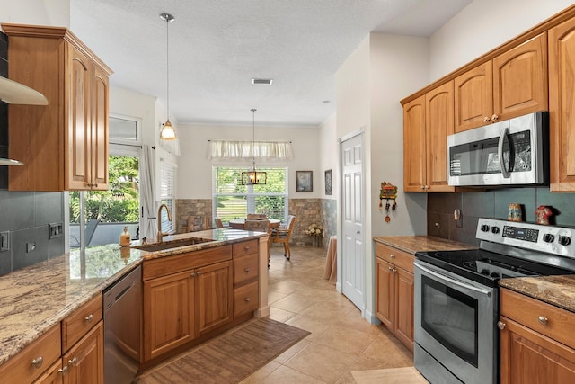 1200 SW Arrowhead Ct, Palm City, FL 34990 - kitchen featuring stainless steel appliances, light stone countertops, hanging light fixtures, light tile patterned flooring, and brown cabinets