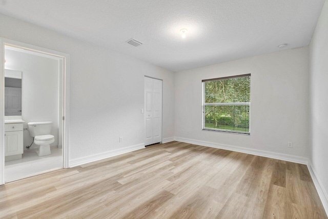 8183 Emerald Winds Cir, Boynton Beach, FL 33473 - unfurnished bedroom with light wood-style flooring, ensuite bath, a closet, and a textured ceiling