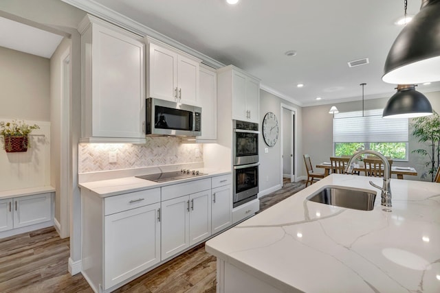 4610 SW Ardsley Dr, Stuart, FL 34997 - kitchen with stainless steel appliances, white cabinetry, backsplash, hanging light fixtures, and light wood-style floors