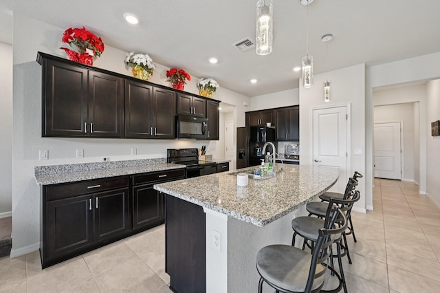 2808 Troubadour St, Palm Springs, FL 33406 - kitchen with black appliances, light tile patterned floors, an island with sink, light stone counters, and a breakfast bar area